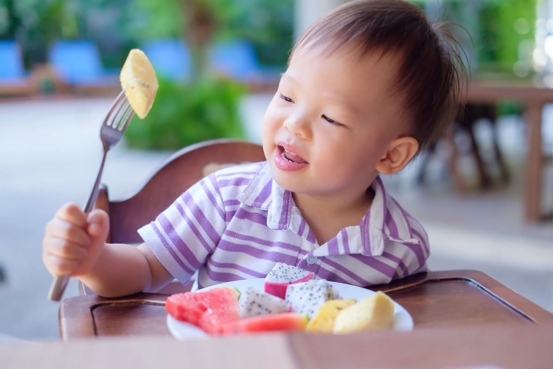 Criança pequena comendo frutas sozinha em cadeira alta